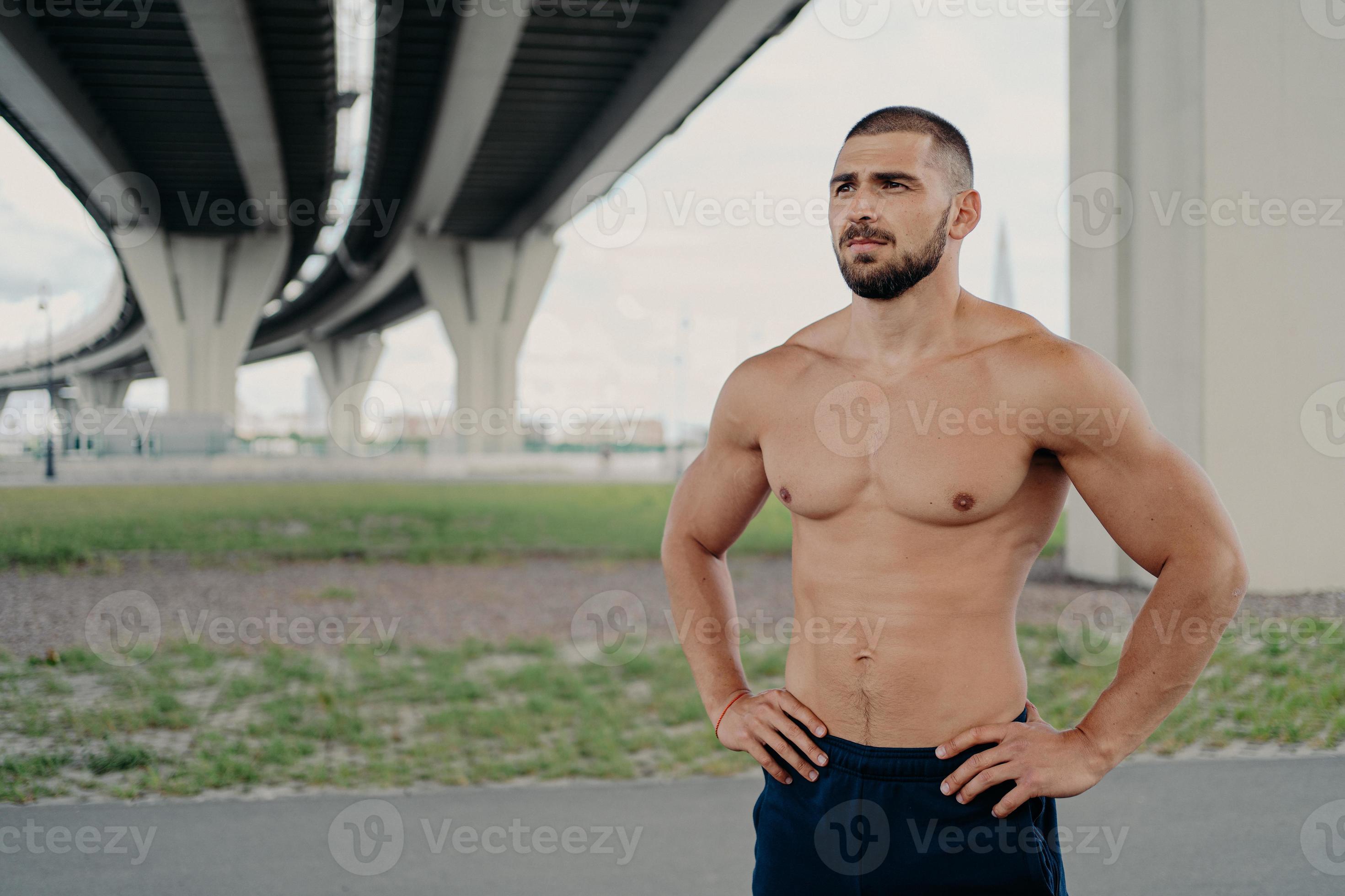 Photo Of Shirtless Handsome Bearded Man With Naked Torso Poses Outdoor Keeps Hands On Waist