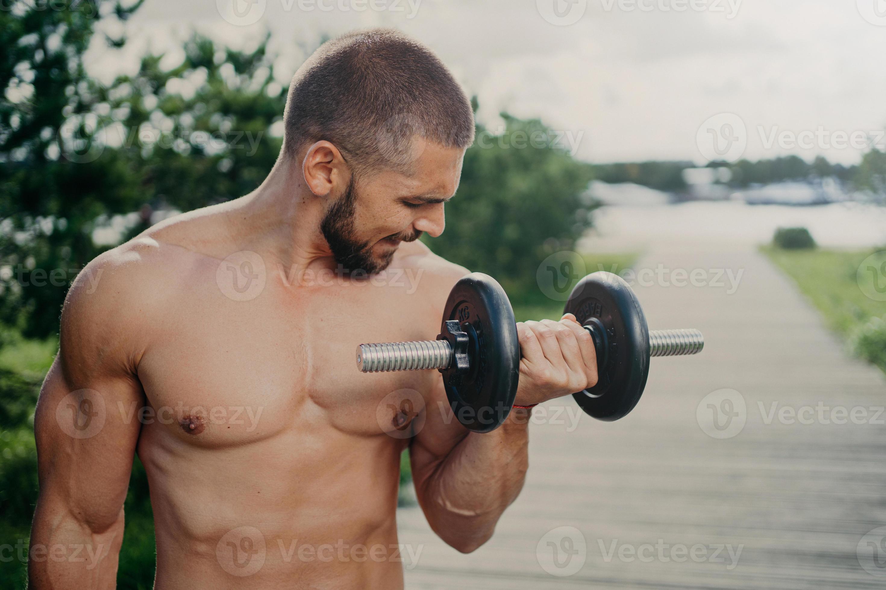 Outdoor Shot Of Strong Muscular Man With Naked Torso Lifts Heavy Barbell And Trains Muscles Has