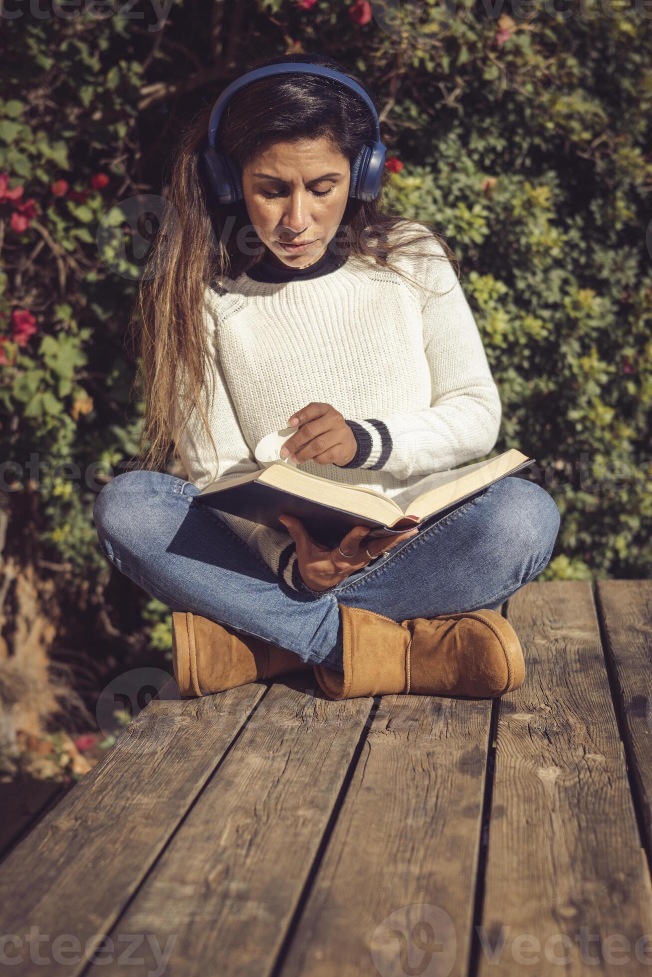 Latina Woman Sitting Outdoors Listening To Music And Reading Stock Photo At Vecteezy
