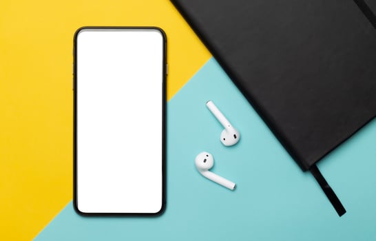 Smartphone and earbuds on yellow and blue background photo