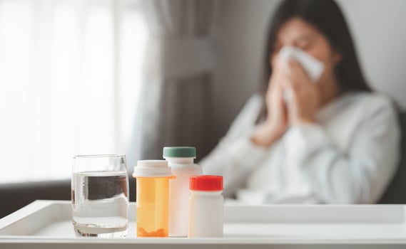 Medicines and glass of water with sick woman in background photo