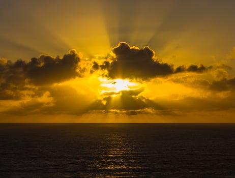 Setting sun through clouds over the ocean photo