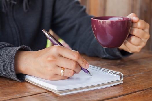 Person taking notes and holding a coffee photo