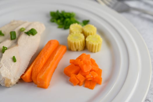 Steamed chicken breast on a white plate with spring onions, baby corn and carrots photo