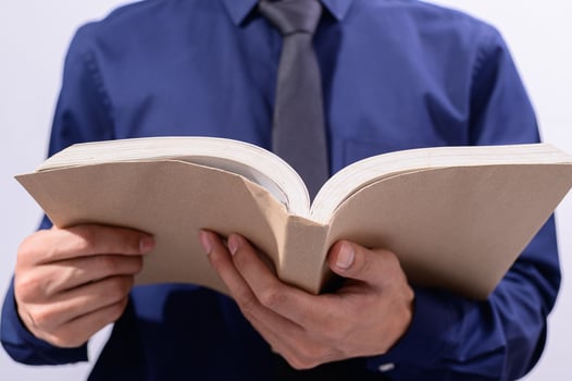 A man in a blue shirt and tie is holding an open book photo