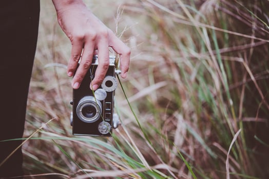 Close-up of a young woman's hand holding a retro camera in a field photo
