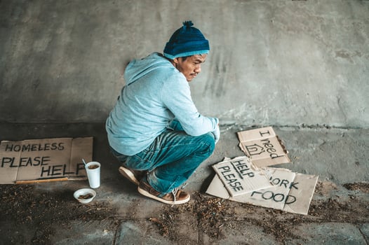 Beggar sitting under a bridge with cardboard signs for help photo