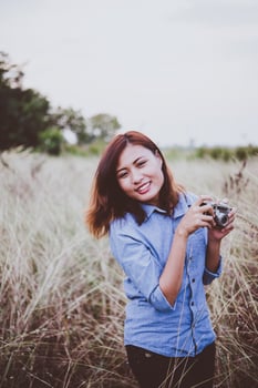 Happy young hipster woman with vintage camera in field photo
