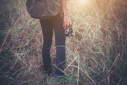 Vintage tone image of young hipster woman with backpack walking in a meadow photo