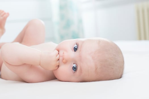 Little baby girl lying with hand in mouth photo