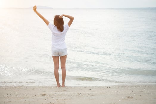 Rear of young woman standing stretch her arms in the air on the beach with bare feet photo