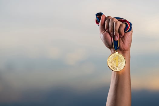 Hand holding gold medal on against cloudy twilight sky background photo