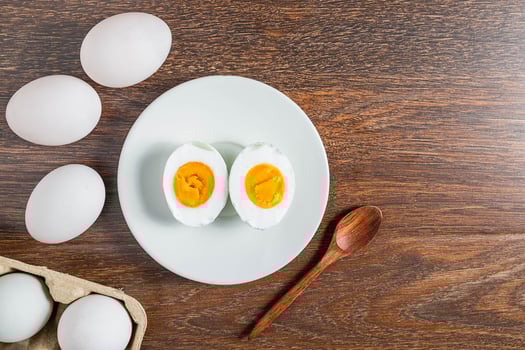 Halved hard-boiled duck egg on a white plate next to whole eggs on a wooden table photo