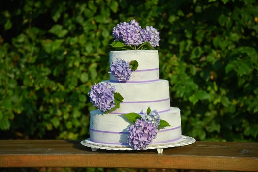 A photo of a wedding cake with violet colored flowers hydrangeas