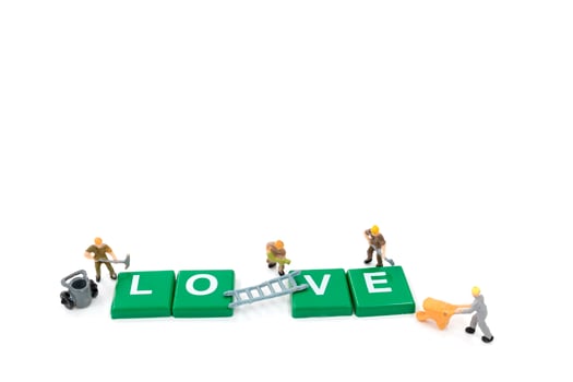 Miniature workers building the word love on a white background photo