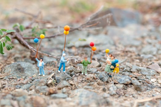 Miniature family walking in a field with balloons, happy family time concept photo