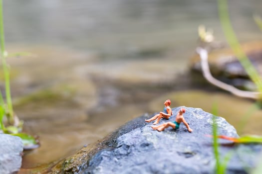Miniature people wearing swimsuits sunbathing on a rock, travel concept photo