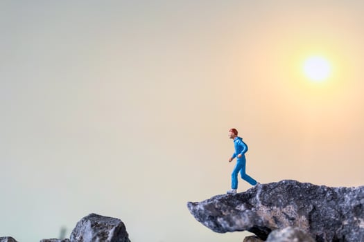Miniature people running on a rock cliff with nature background, health and lifestyle concept photo