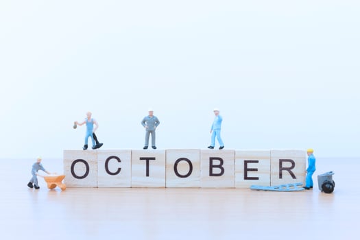 Miniature people working on wooden blocks with the word October on a wooden floor photo