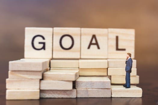 Miniature businessman standing on wooden blocks with the word Goal, business career growth concept photo