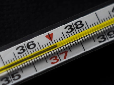 Close-up of a mercury thermometer with a high reading of 37.1 body temperature, against a black background photo