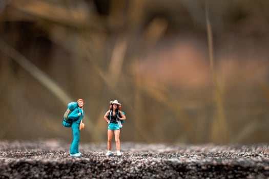 Miniature backpackers standing on a concrete floor with a bokeh nature background photo