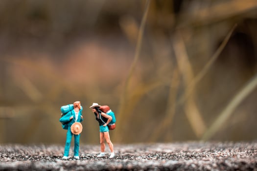 Miniature backpackers standing on a concrete floor with a bokeh nature background photo