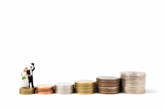 Miniature bride and groom on a stack of coins on a white background photo