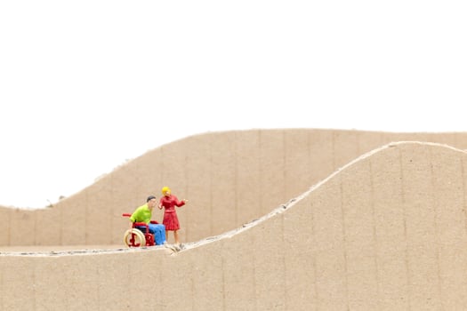 Miniature man in a wheelchair and woman on a cardboard cutout isolated on a white background photo