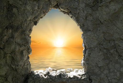 Orange sunset over a body of water seen through a window in a stone wall photo