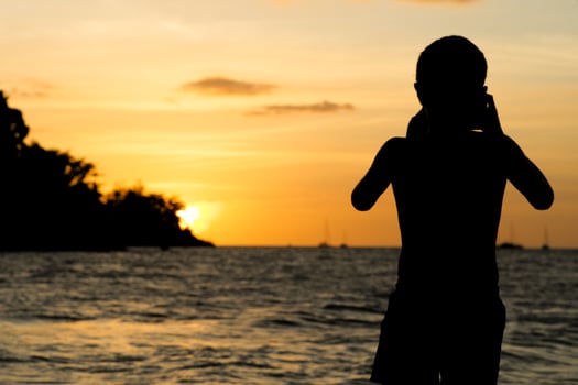 Silhouette portrait of young boy taking a seascape scene on the beach with light of sunset photo