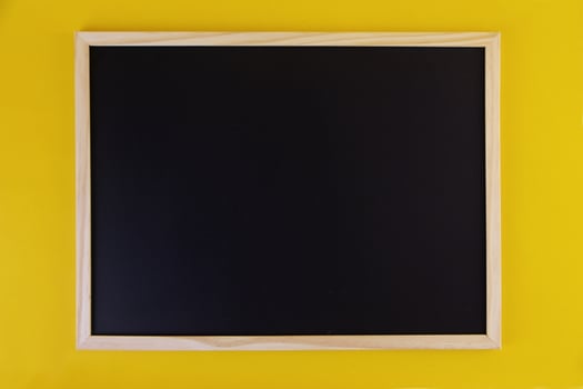 Empty black chalkboard on yellow background. Front view on black chalkboard with wooden frame. Empty copy space on flat panel. photo