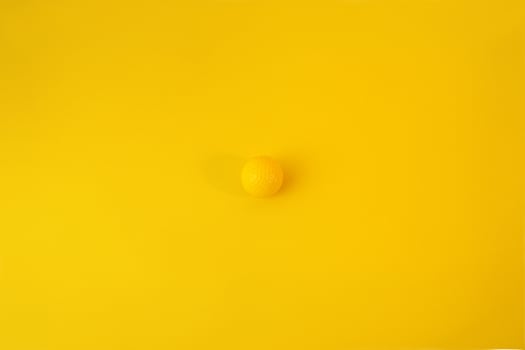 Yellow golf ball isolated on yellow background. Concept of minimalism. photo