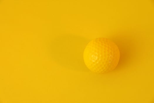 Yellow golf ball isolated on yellow background. Monotone concept. Clean copy space. photo
