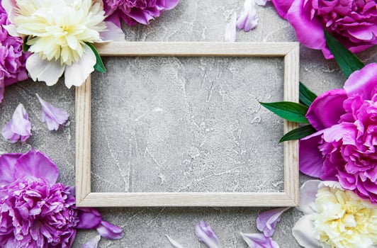Wooden frame surrounded by beautiful pink peonies on a grey concrete background photo