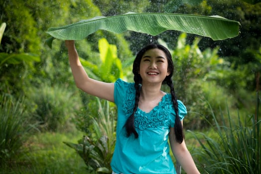 Asian woman with black hair holding a banana leaf in the rain photo