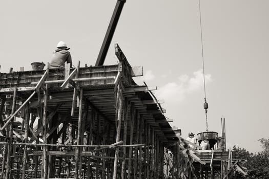 Monochrome picture of workers pouring mixed cement from a steel bucket hanging from a crane photo