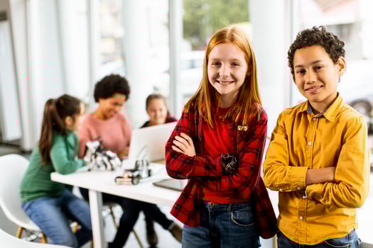 Best friends standing in front of kids programming electric toys and robots at robotics classroom photo