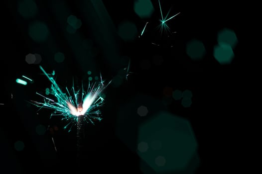 Sparkler in turquoise and white light on a black background photo