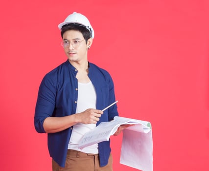Portrait of young architect wearing a white helmet holding a construction plan on a red background photo