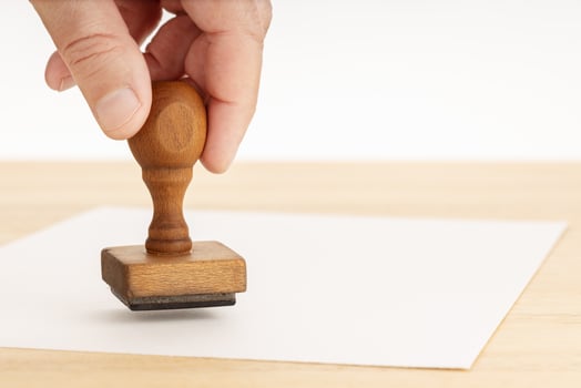 Hand holding a rubber stamp and blank paper on wooden table photo