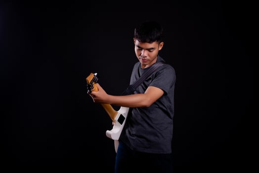 Young man in black leather jacket with electric guitar against black background in studio photo