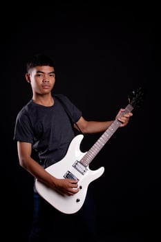 Young man in black leather jacket with electric guitar against black background in studio photo