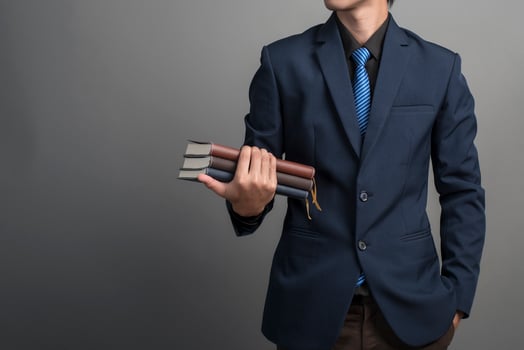 Close up of businessman in blue suit holding books on gray background photo