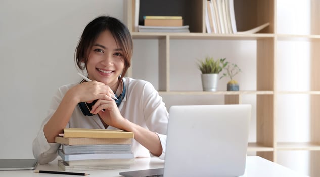 Smiling Asian woman working on the desk with books and laptop computer photo