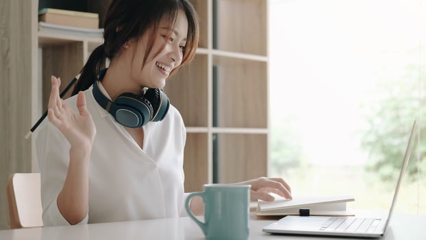 Happy young Asian businesswoman waving hands to greet partners during a video conference with her team photo