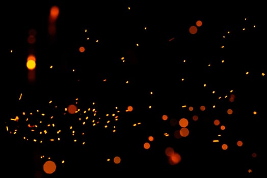 Particles of burning embers fly and glow isolated in the night sky. Bright yellow sparks on a black background, yellow bright round bokeh. photo