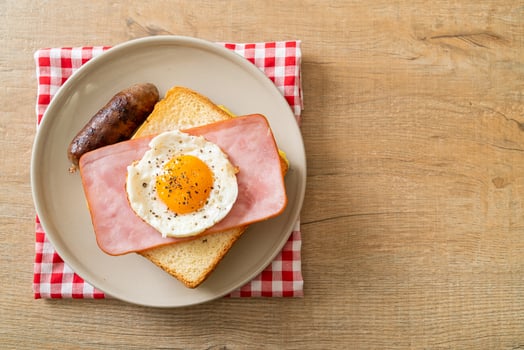 Homemade bread toasted cheese, topped ham, and fried egg with pork sausage for breakfast photo