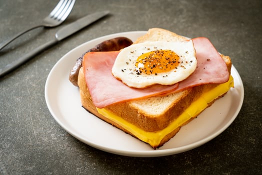 Homemade bread toasted cheese, topped ham, and fried egg with pork sausage for breakfast photo