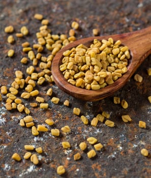 Fenugreek seeds in wooden spoon on textured background photo